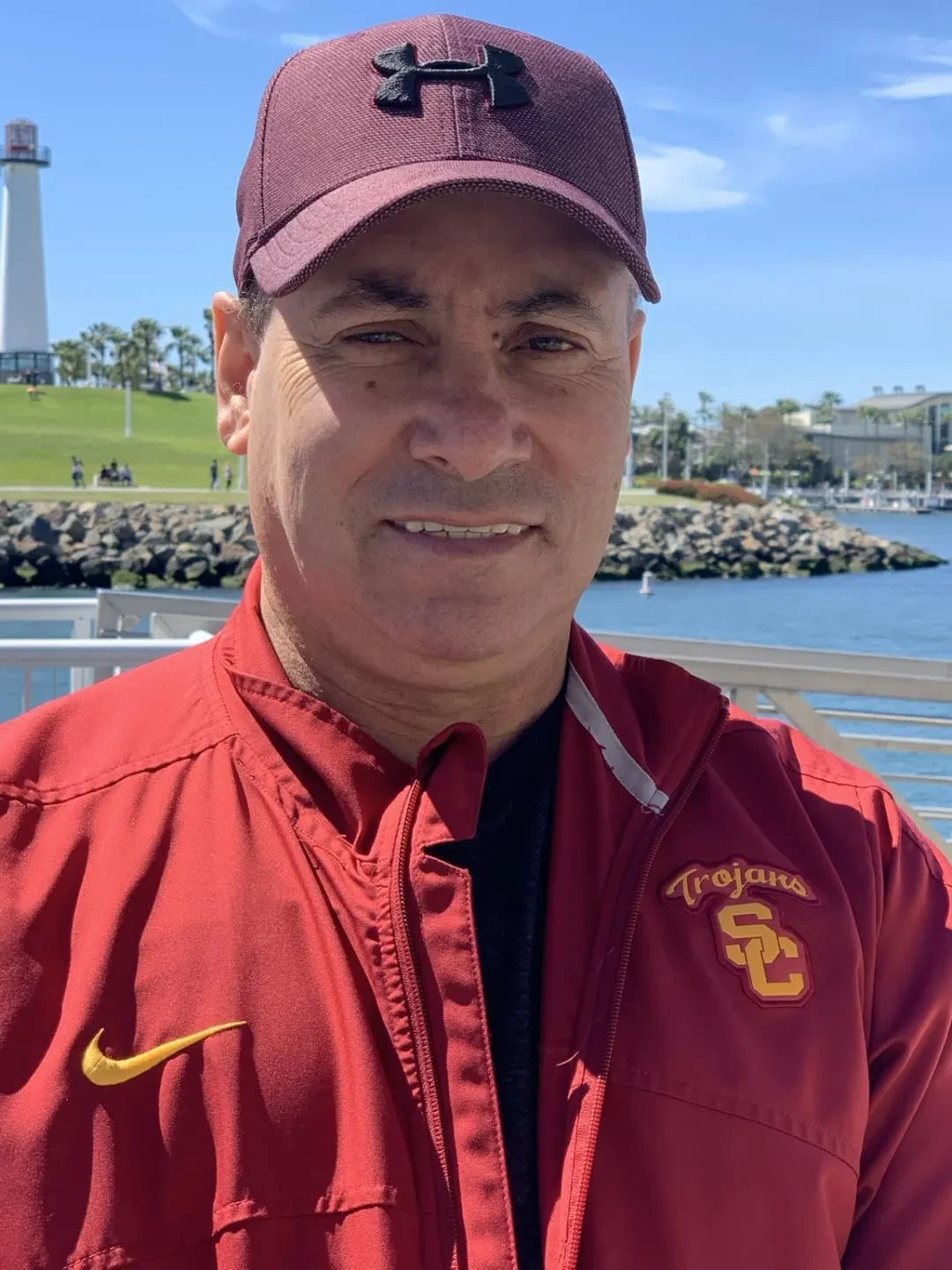 Ted Vigo wearing a red USC Trojans jacket and burgundy cap by the waterfront